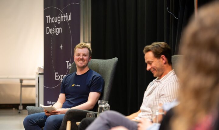 Harry, the Managing Director of Unfold is sat next to another man, Clem, looking happy and smiling. They are sat side by side in front of an audience
